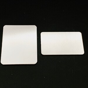 May include: Two white rectangular blank cards on a black textured surface. The larger card is slightly larger than the smaller card.
