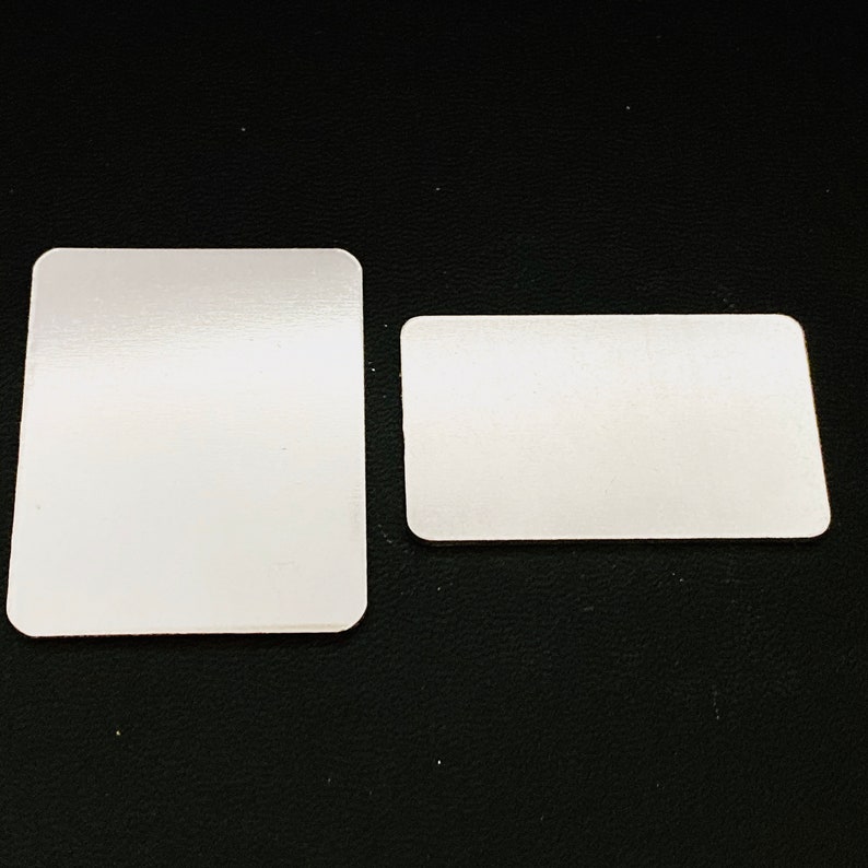 May include: Two white rectangular blank cards on a black textured surface. The larger card is slightly larger than the smaller card.