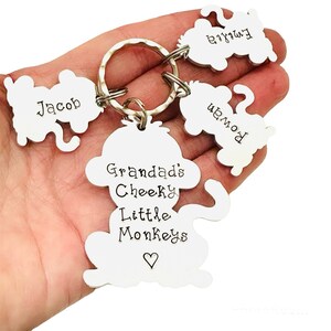 Puede incluir: Un llavero de plata con un gran dije de mono que dice "Granddad's Cheeky Little Monkeys" con un coraz&oacute;n. Hay tres dijes de mono m&aacute;s peque&ntilde;os unidos al anillo, cada uno con un nombre: Jacob, Emma y Aiden.