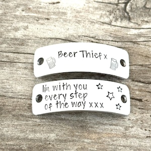 May include: Two curved, rectangular silver-toned metal tags with holes on each end. The top tag features the text "Beer Thief x" with two beer mug icons. The bottom tag features the text "I'm with you every step of the way xxx" with four stars.