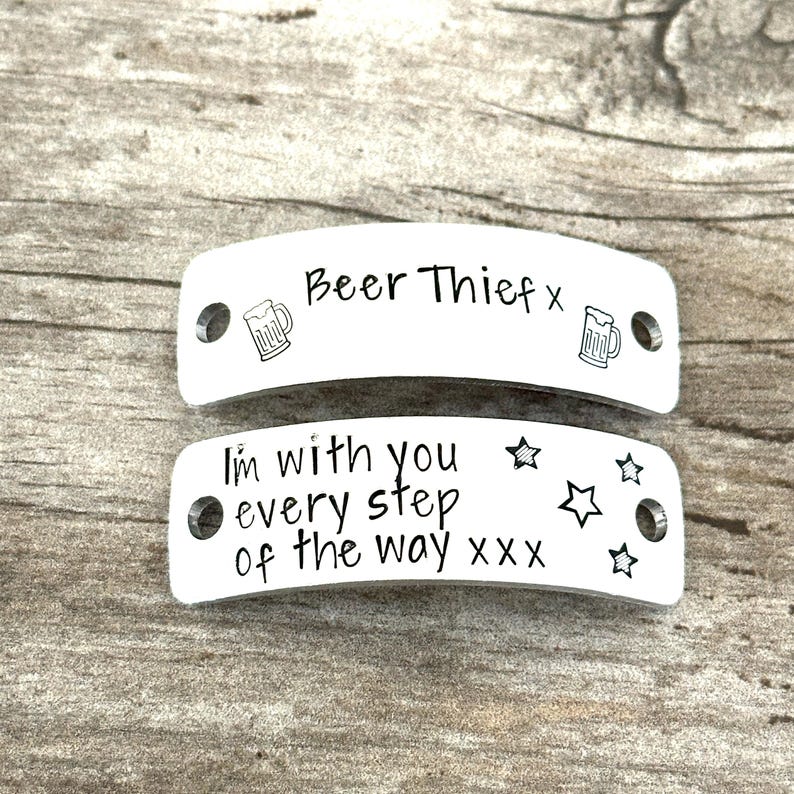 May include: Two curved, rectangular silver-toned metal tags with holes on each end. The top tag features the text "Beer Thief x" with two beer mug icons. The bottom tag features the text "I'm with you every step of the way xxx" with four stars.