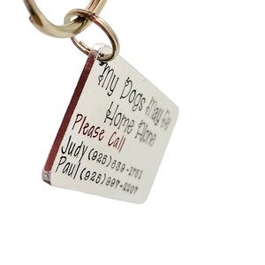 May include: Silver dog tag keyring with a red border. The tag reads "My Dogs May Be Home Alone Please Call Judy (925) 639-1781 Paul (925) 997-2207".