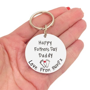 Peut inclure: Porte-cl&eacute;s argent&eacute; avec une &eacute;tiquette ronde qui dit "Happy Fathers Day Daddy Love From Bump X" avec un c&oelig;ur rouge et deux empreintes de pas.