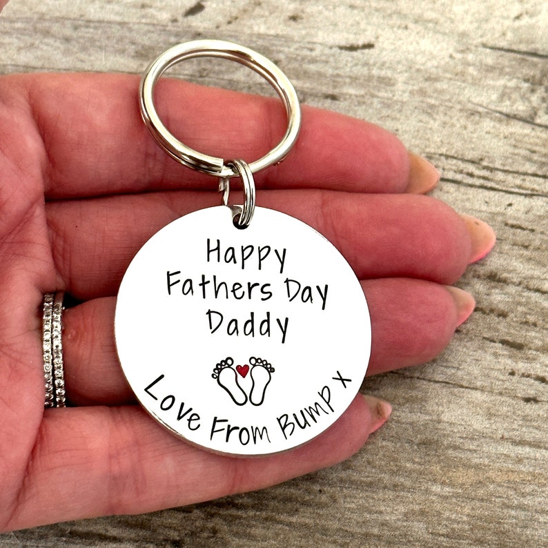 Peut inclure: Porte-cl&eacute;s argent&eacute; avec une &eacute;tiquette ronde qui dit "Happy Fathers Day Daddy Love From Bump X" avec un petit c&oelig;ur rouge et deux empreintes de pas.