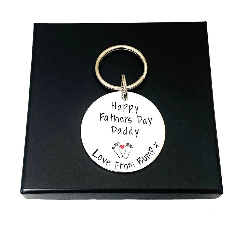 Peut inclure: Un porte-cl&eacute;s argent&eacute; avec une &eacute;tiquette ronde qui dit "Happy Fathers Day Daddy Love From Bump x" avec un petit c&oelig;ur rouge et deux empreintes de pas.