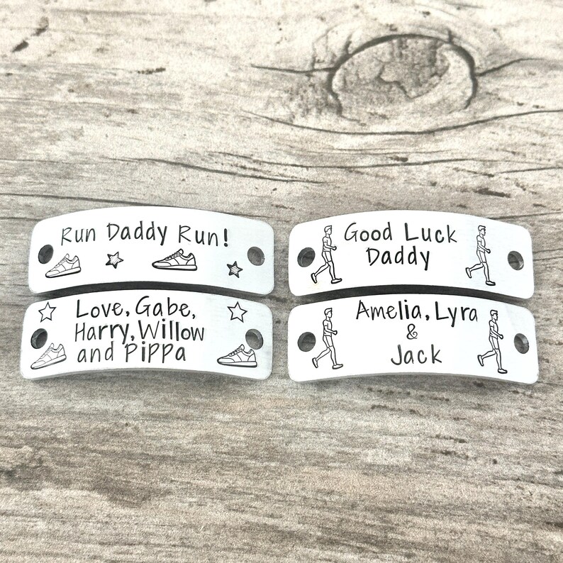 May include: Four rectangular silver-toned metal tags with rounded edges and two holes for attachment. The tags feature engraved black text and graphics including running shoes, stars, and figures of people running, with personalized names.