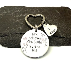 Pode incluir: Um porta-chaves de metal prateado com um anel em forma de cora&ccedil;&atilde;o e um pendente redondo gravado com o texto She Believed She Could So She Did, acompanhado de motivos florais e borboletas e um pequeno cora&ccedil;&atilde;o com 1 Stone.