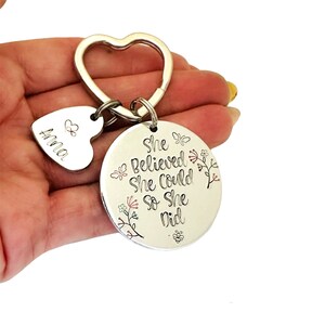 Pode incluir: Um porta-chaves de metal prateado com um anel em forma de cora&ccedil;&atilde;o, um pequeno pendente em forma de cora&ccedil;&atilde;o gravado com o nome Anna e um s&iacute;mbolo de cora&ccedil;&atilde;o, e um grande disco circular gravado com o texto She Believed She Could So She Did, borboletas e flores.