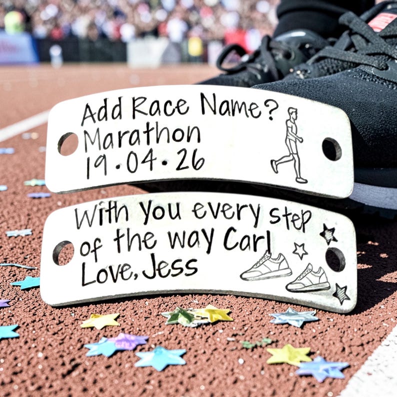 May include: Two rectangular silver-toned metal shoe tags with rounded corners and two holes each. The top tag reads Add Race Name? Marathon 19.04.26 with a runner icon. The bottom tag reads With you every step of the way Carl Love, Jess with shoe icons.