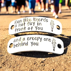 May include: Two white metal running shoe tags with black text that reads "Run like there's a hot guy in front of you" and "and a creepy one behind you". Each tag has a running figure graphic.
