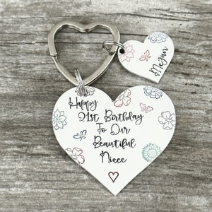 May include: White heart-shaped keychain with the text "Happy 21st Birthday to Our Beautiful Niece" and a small heart at the bottom. A smaller heart-shaped tag with the name "Megan" is attached to the keychain.