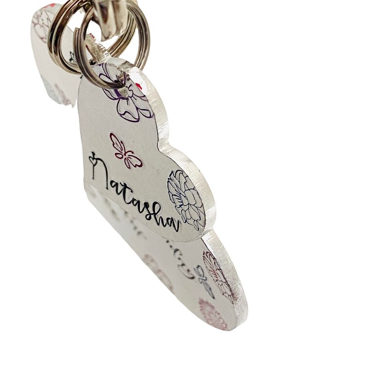 May include: Silver heart-shaped keychain with a floral design and the name "Natasha" engraved on it.