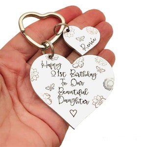 May include: White heart-shaped wooden keychain with the text "Happy 21st Birthday To Our Beautiful Daughter" and a smaller heart-shaped keychain with the name "Renee" engraved on it.