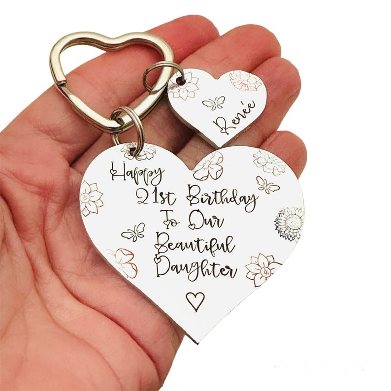 May include: White heart-shaped wooden keychain with the text "Happy 21st Birthday To Our Beautiful Daughter" and a smaller heart-shaped keychain with the name "Renee" engraved on it.