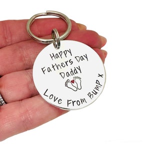 Peut inclure: Porte-cl&eacute;s argent&eacute; avec une &eacute;tiquette ronde qui dit "Happy Fathers Day Daddy Love From Bump" avec un c&oelig;ur rouge et deux empreintes de pas.