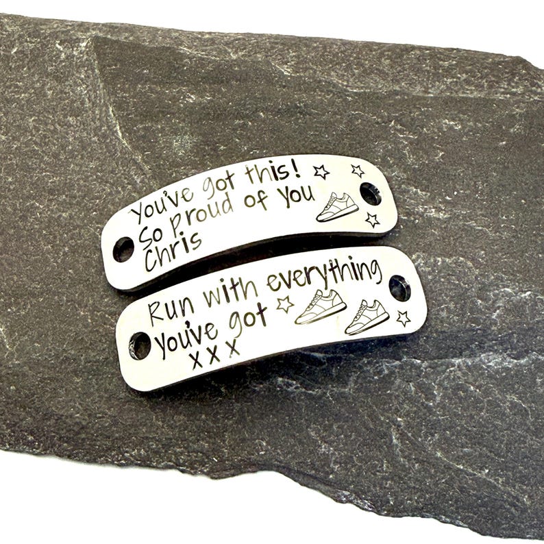 May include: Two silver-toned metal shoe tags with curved edges and two holes for lacing. The top tag is engraved with "You've got this! So proud of you Chris" and a sneaker icon. The bottom tag reads "Run with everything you've got XXX" with sneaker icons.