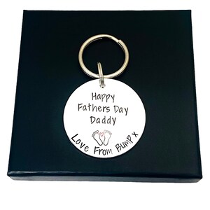 Peut inclure: Porte-cl&eacute;s rond blanc avec le texte "Happy Fathers Day Daddy Love From Bump x" et une petite image de deux empreintes de pieds de b&eacute;b&eacute; avec un c&oelig;ur entre elles.