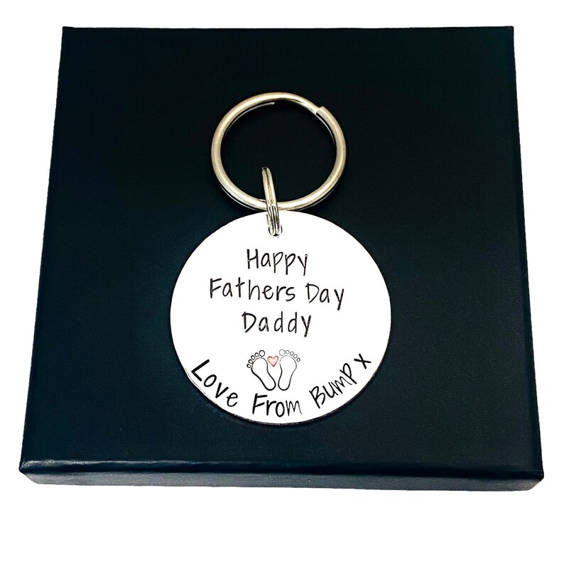 Peut inclure: Porte-cl&eacute;s rond blanc avec le texte "Happy Fathers Day Daddy Love From Bump x" et une petite image de deux empreintes de pieds de b&eacute;b&eacute; avec un c&oelig;ur entre elles.