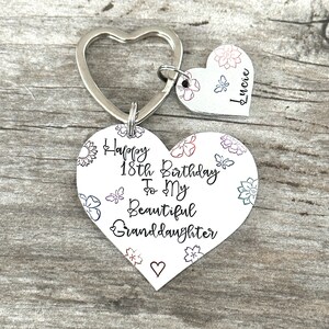 May include: Silver heart-shaped keychain with a message that reads "Happy 18th Birthday To My Beautiful Granddaughter" with floral designs. A smaller heart-shaped tag with the name "Lucille" is attached to the keychain.