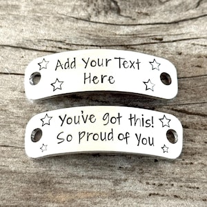 May include: Two silver-colored metal tags with rounded edges. The top tag reads "Add Your Text Here" and is decorated with star shapes. The bottom tag says "You've got this! So proud of You" and also has star shapes.