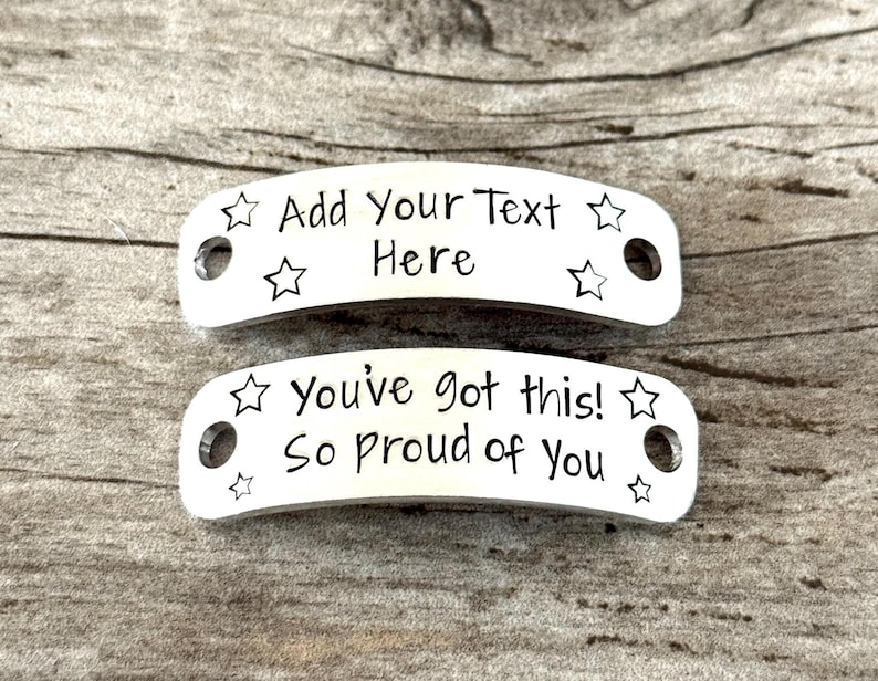 May include: Two silver-colored metal tags with rounded edges. The top tag reads "Add Your Text Here" and is decorated with star shapes. The bottom tag says "You've got this! So proud of You" and also has star shapes.