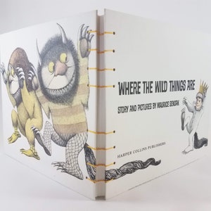 Może przedstawiać: Biała książka z ż&oacute;łtym grzbietem i czarno-białą ilustracją potwora na okładce. Tytuł książki to "Where the Wild Things Are" z podtytułem "Story and Pictures by Maurice Sendak".