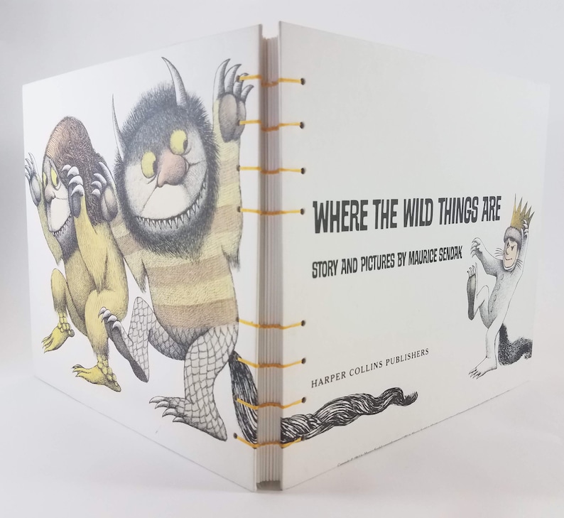 Może przedstawiać: Biała książka z ż&oacute;łtym grzbietem i czarno-białą ilustracją potwora na okładce. Tytuł książki to "Where the Wild Things Are" z podtytułem "Story and Pictures by Maurice Sendak".