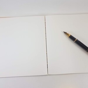 Może przedstawiać: Pusty notes z czarnym i złotym długopisem leżącym na prawej stronie.