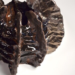 May include: A dark brown ceramic sculpture with a textured, organic shape. The sculpture has a glossy finish and appears to be made of multiple pieces.