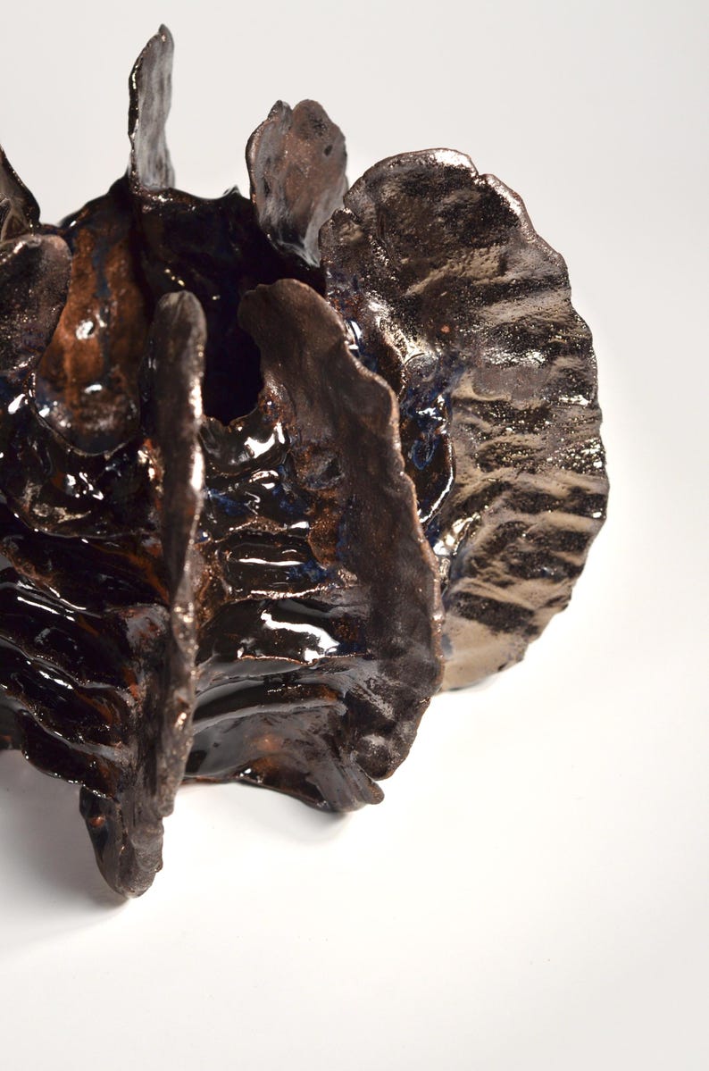 May include: A dark brown ceramic sculpture with a textured, organic shape. The sculpture has a glossy finish and appears to be made of multiple pieces.