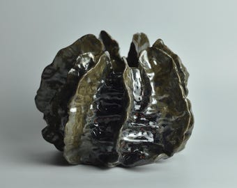 May include: A dark green ceramic vase with a unique, organic shape resembling a cluster of leaves. The vase has a glossy finish and a textured surface.