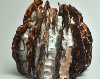 May include: A textured ceramic vase with a unique, organic shape. The vase features a combination of dark brown, light brown, and white glaze, creating a layered effect. The design has a rough, uneven surface, adding to its artistic appeal. The vase is a decorative item.
