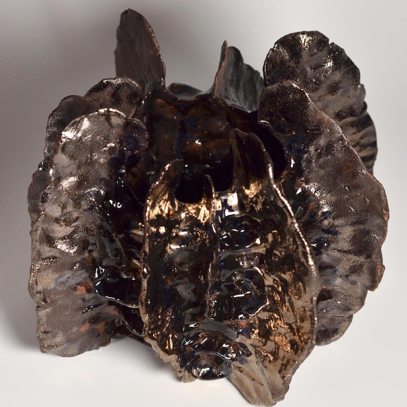 May include: A ceramic sculpture with a dark brown and metallic finish. The sculpture has a unique, organic shape with multiple layers and textures.