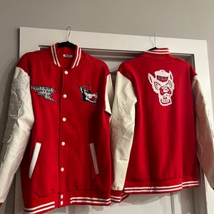 Può includere: Sono mostrate due giacche varsity rosse e bianche. Le giacche hanno maniche bianche e un corpo rosso con strisce bianche sul fondo. Una giacca ha il testo "DON'T GIVE UP DON'T EVER GIVE UP". L'altra giacca ha un logo di lupo.