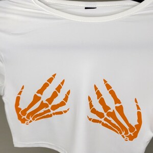 May include: White crop top with orange skeleton hand print design.
