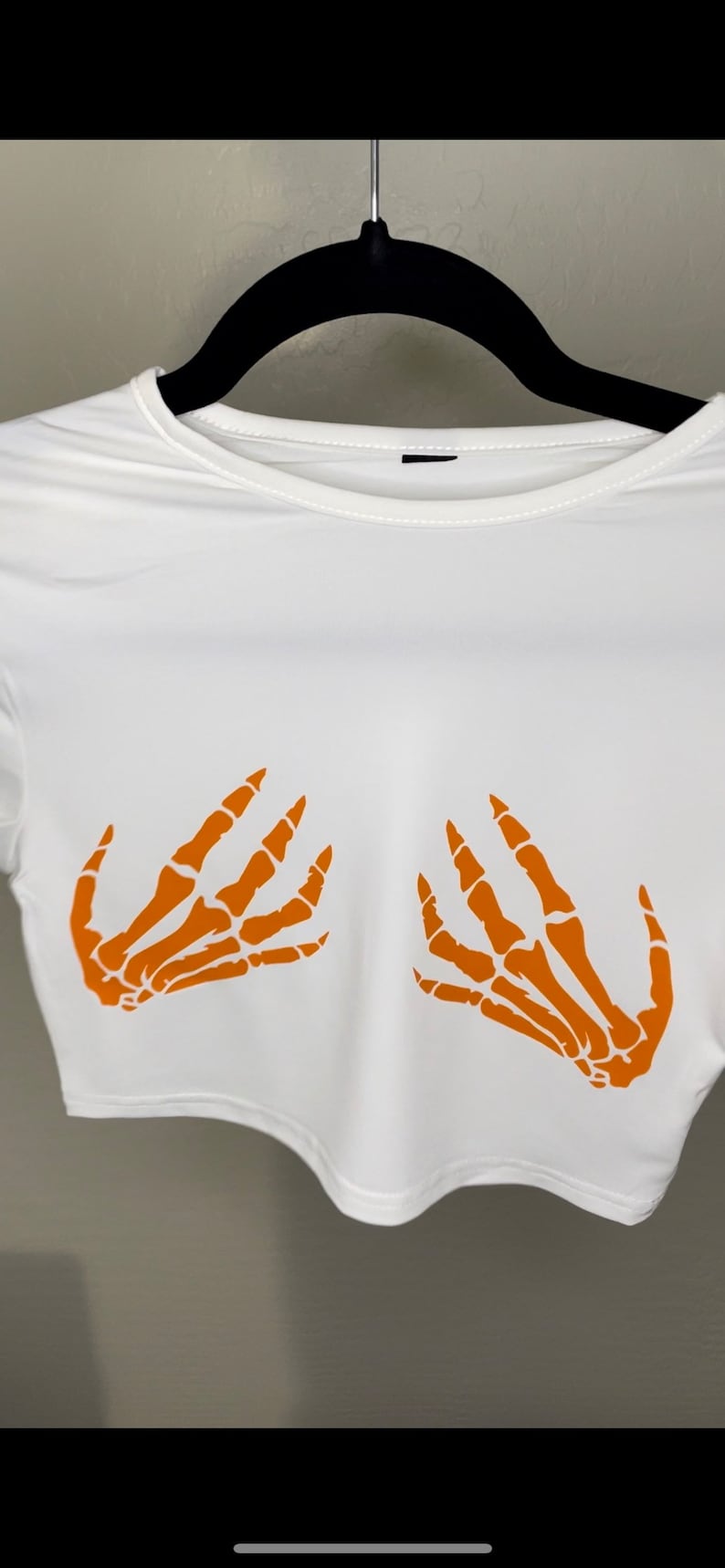 May include: White crop top with orange skeleton hand print design.