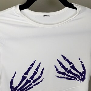 May include: White crop top with a skeleton hand design in dark purple on the front.
