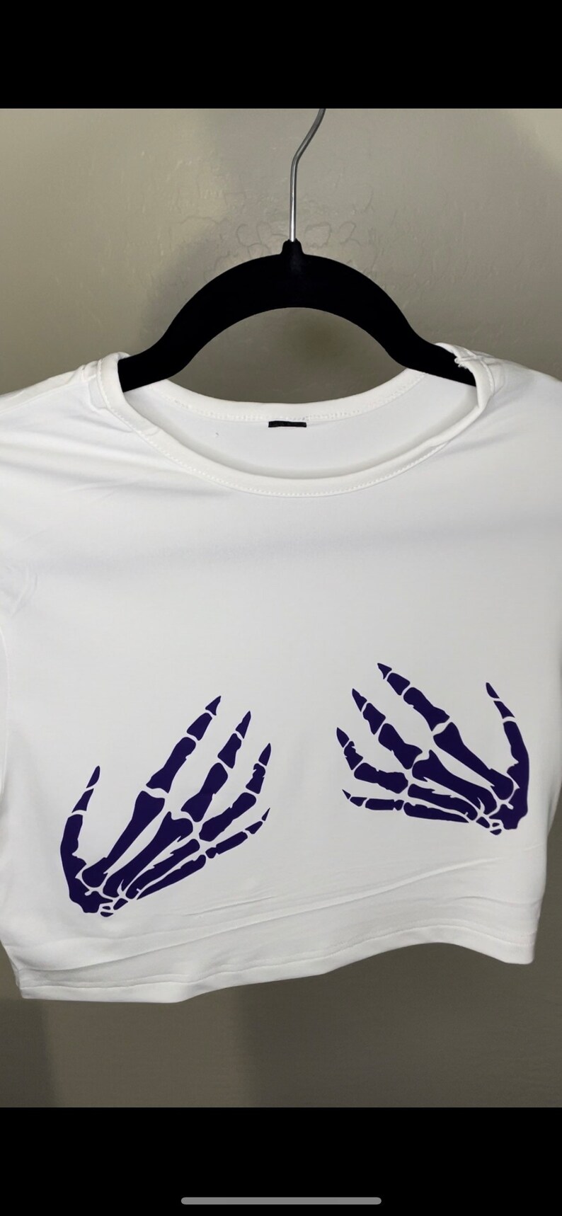 May include: White crop top with a skeleton hand design in dark purple on the front.