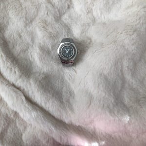 May include: A silver wristwatch with a black face and silver hands. The watch is on a white fluffy surface.