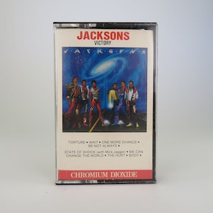 May include: A cassette tape of the Jackson 5's album "Victory". The cover features a blue and purple galaxy background with the five brothers walking in a line. The album title is printed in white letters on a black background. The cassette tape is labeled "Chromium Dioxide".