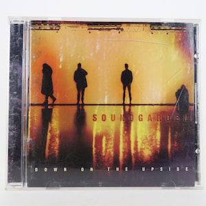 May include: A CD case with a yellow and orange background featuring the band Soundgarden. The band's name is printed in white letters and the album title "Down on the Upside" is printed in white letters at the bottom of the case.