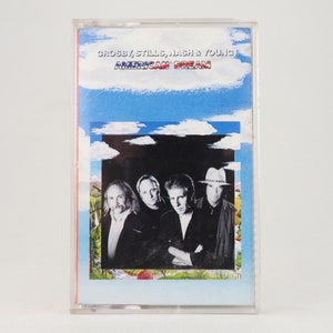 Könnte beinhalten: Eine Kassette mit einem Hintergrund aus blauem Himmel und Wolken. Die Vorderseite der Kassette zeigt ein Schwarzweißfoto von Crosby, Stills, Nash & Young. Der Text "Crosby, Stills, Nash & Young" und "American Dream" ist in Weiß auf der Kassette gedruckt.