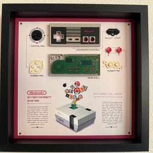 Könnte beinhalten: Ein gerahmtes Display mit einem zerlegten Nintendo Entertainment System Controller, dessen Komponenten als Control Pad, Logicboard Assembly, Rubber Pad und Rear Shell beschriftet sind. Darunter eine Illustration der Konsole mit Spielsymbolen.