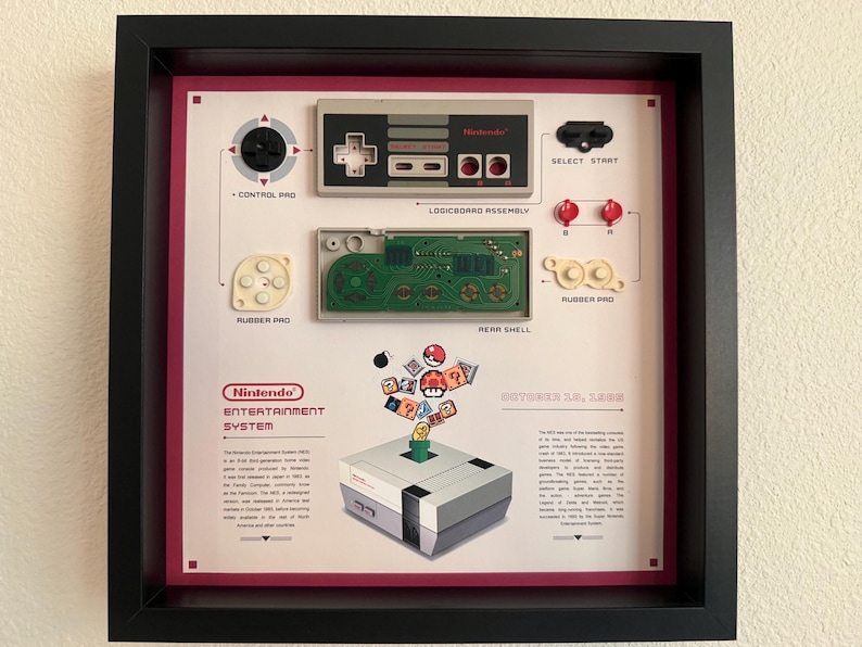 May include: A framed display featuring a disassembled Nintendo Entertainment System controller with components labeled as control pad, logicboard assembly, rubber pad, and rear shell. Below, an illustration of the console with game icons.