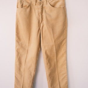 Peut inclure: Un pantalon en velours côtelé marron clair suspendu à un cintre en bois. Le pantalon a une jambe droite et une coupe classique.
