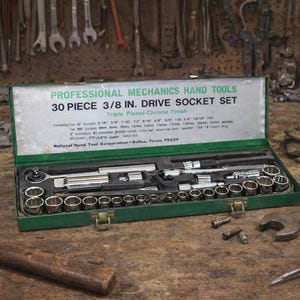 May include: A green metal toolbox labeled "PROFESSIONAL MECHANICS HAND TOOLS" contains a 30-piece 3/8 in. drive socket set. The set includes various sockets, ratchets, and extensions. The toolbox is open, revealing the tools inside. The background shows other tools.