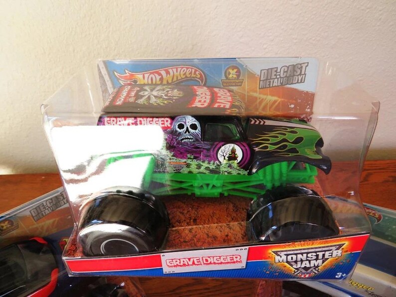 May include: A Hot Wheels Grave Digger monster truck toy in its original packaging. The die-cast metal body truck features a skull graphic, green flames, and a green chassis. The packaging includes the Monster Jam logo.