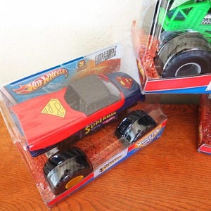 May include: A die-cast metal Hot Wheels Superman monster truck in its original packaging. The truck features a red and blue design with the Superman logo. The packaging includes the Hot Wheels logo and the word "Superman".