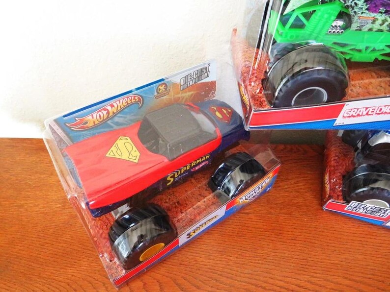 May include: A die-cast metal Hot Wheels Superman monster truck in its original packaging. The truck features a red and blue design with the Superman logo. The packaging includes the Hot Wheels logo and the word "Superman".
