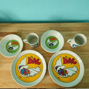 May include: A set of three ceramic mugs with a speckled, matte finish. The mugs are in shades of cream, light gray, and dark gray. Each mug has a simple, minimalist design and a rounded handle.